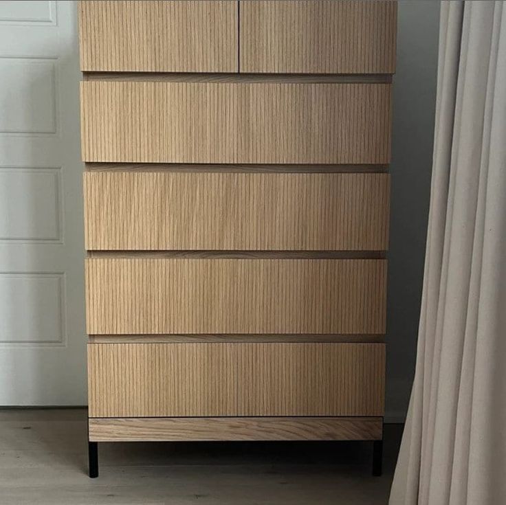 a tall wooden dresser sitting next to a white door in a room with curtains on the windowsill