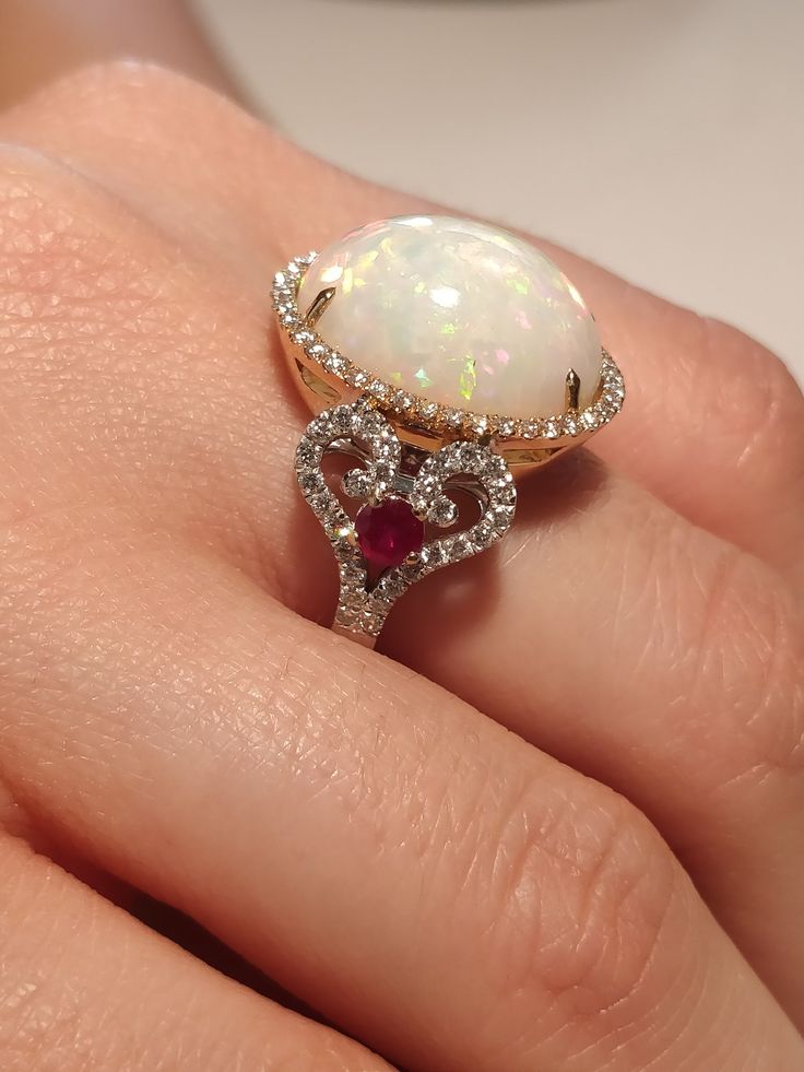 a woman's hand holding an opal and diamond ring