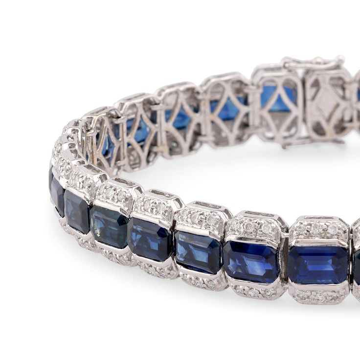 Center Stone: 29 Emerald Cut Blue SapphireWeight: 22 CaratsAccent Stone: 174 Round Brilliant Cut DiamondsWeight: 2 CaratsColor: GClarity: VSMetal: 18K White GoldEra: VintageCirca: 1990sSize: 7 1/8 inches in lengthGram weight: 24.56This stunning vintage bracelet from the 1990s is crafted in luxurious 18K white gold and features 29 vibrant emerald cut blue sapphires, totaling 22 carats. The sapphires are beautifully complemented by 174 sparkling round brilliant cut diamonds, totaling 2 carats, wit Elegant Hand Set Blue Bracelet, Elegant Blue Hand Set Bracelets, Elegant Blue Hand-set Bracelet, Luxury Blue Tennis Bracelet, Wedding Sapphire Diamond Bracelet With 17 Jewels, Blue Diamond Bracelet For Formal Occasions, Luxury Blue Diamond Bracelet With Accents, Classic Sapphire Bracelets For Anniversary, Classic Sapphire Tennis Bracelet For Anniversary