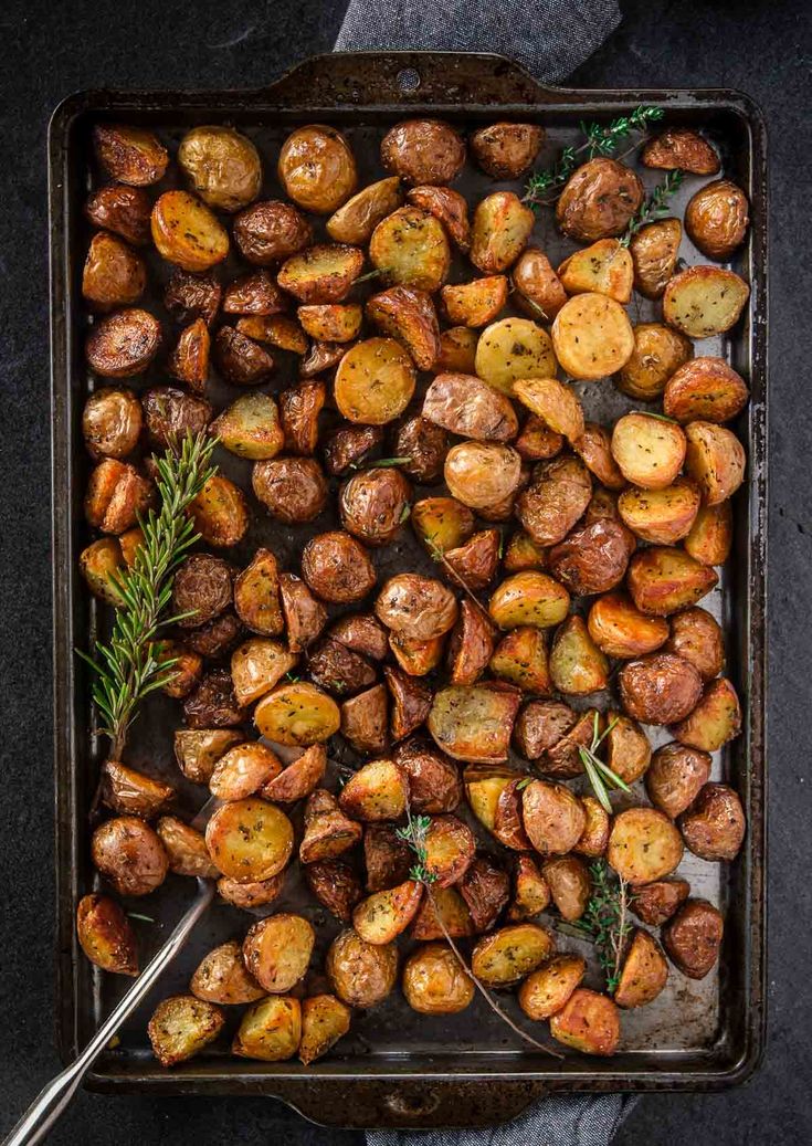 roasted potatoes on a baking sheet with rosemary sprigs and salt in a pan