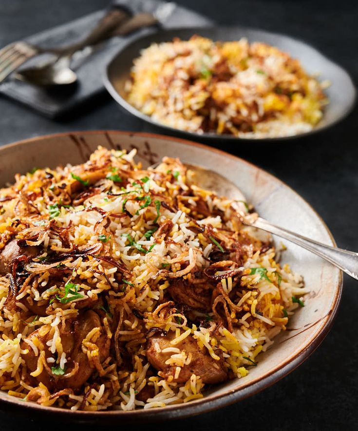 two plates filled with rice and meat on top of a black tablecloth next to silverware