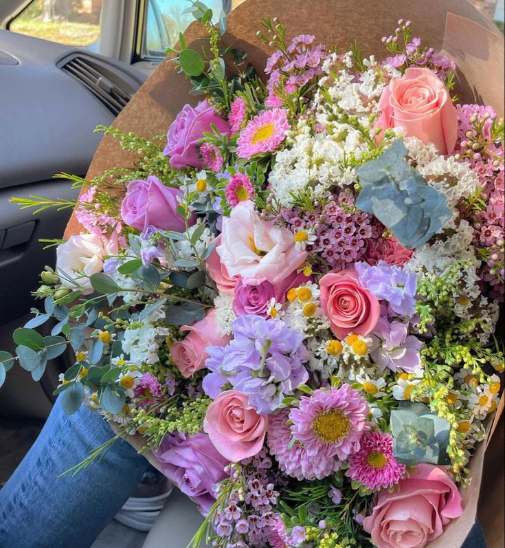 a bouquet of flowers sitting in the back seat of a car with someone holding it