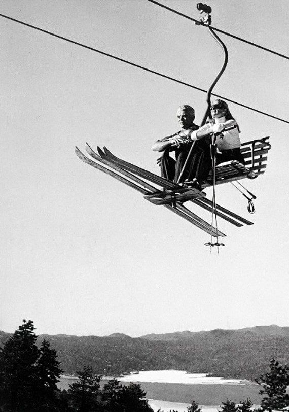 two people are sitting on a ski lift above the water and trees in the background