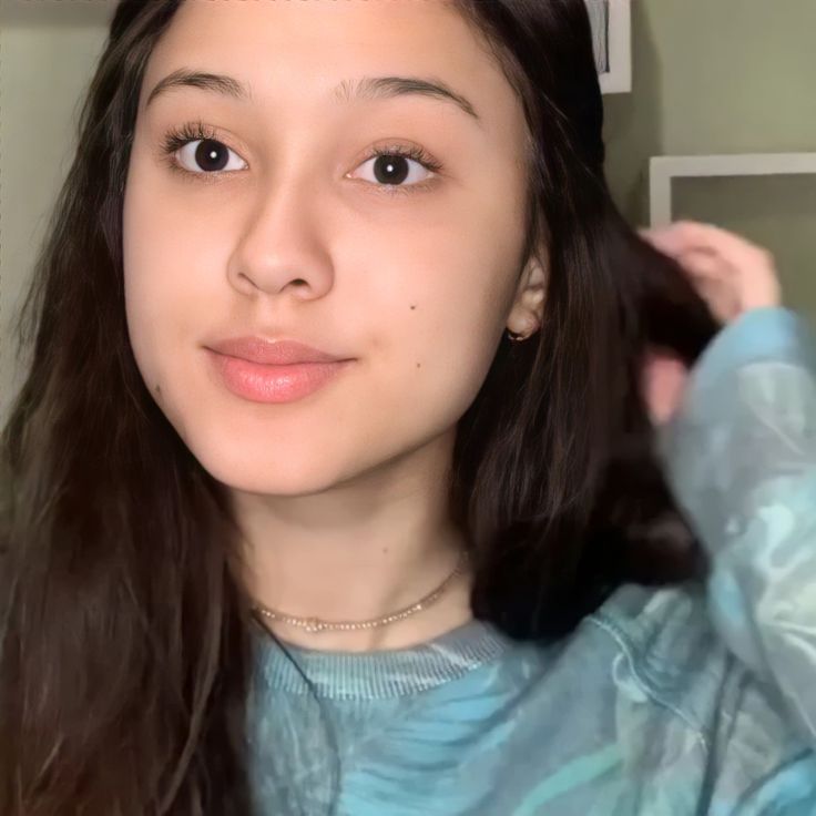 a young woman with long dark hair is looking at the camera while wearing a blue shirt