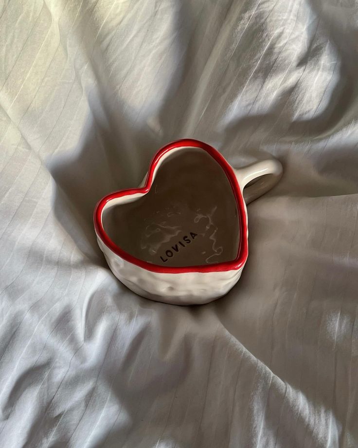 a heart shaped bowl sitting on top of a white bed sheet with the word i love you written on it