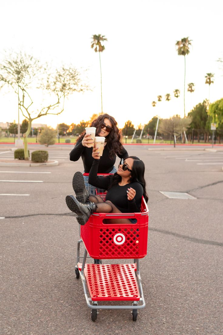 two people sitting on top of a red shopping cart