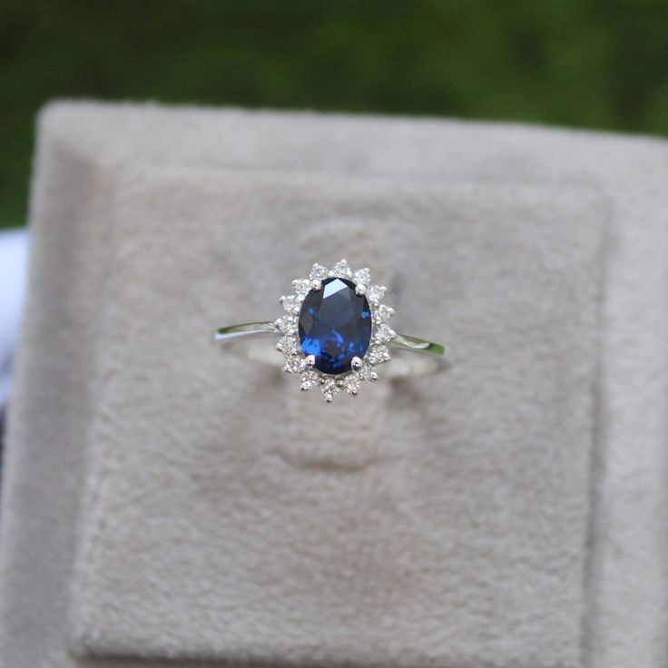 a ring with a blue stone is sitting on top of a white box and some grass in the background