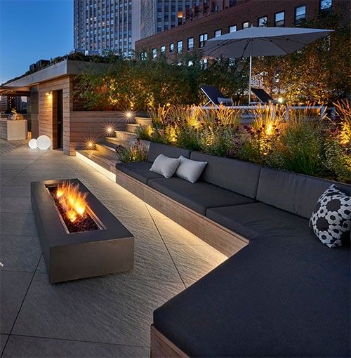 an outdoor fire pit is lit up at night in front of a cityscape