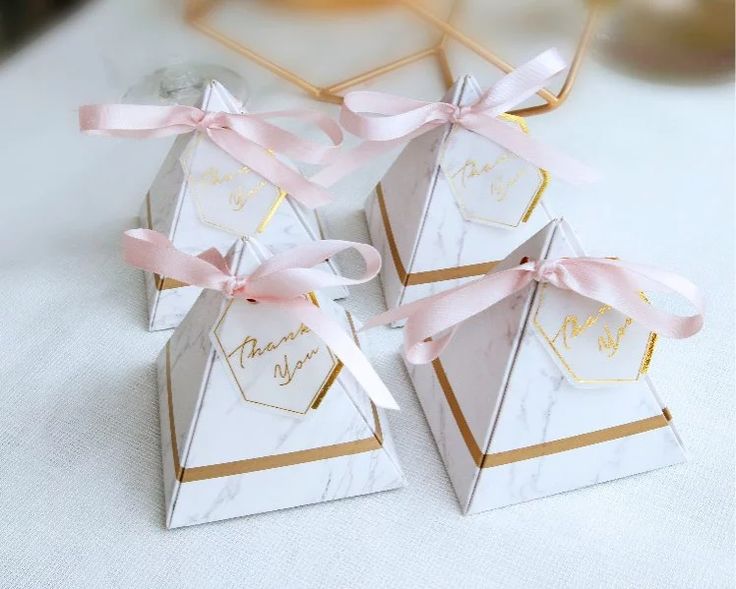 three small white boxes with pink bows on them sitting on a table next to a vase