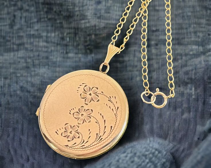 "Description: A wonderful vintage round gold filled locket necklace with an ornately decorated etched front that features three flowers with leaves and curved stems of three different lengths that grow up and curl around the right side of this locket. All round the circular locket front is a fine etched line that frames the floral design. The back of this retro locket is plain with no design and has a shiny finish. The fanned bale is a decorative one with some angled lines.  This larger sized lo Victorian Round Locket Necklace Stamped 14k, Yellow Gold Round Filigree Locket Necklace, Yellow Gold Round Locket Necklace With Filigree, Round Yellow Gold Locket Necklace With Filigree, Classic Round Locket Necklace With Intricate Design, Antique Gold Round Locket Necklace, Hallmarked, Victorian Filigree Round Locket Necklace, Hallmarked Antique Gold Locket Necklace, Ornate Gold Round Locket Necklace