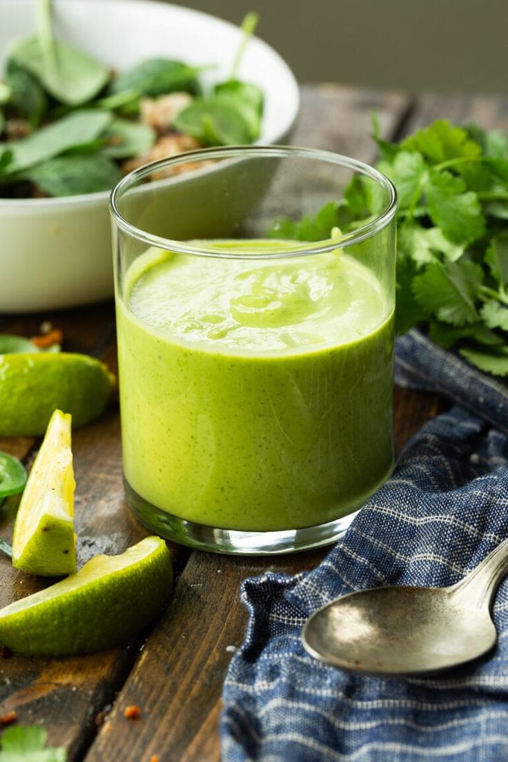 a green smoothie in a glass on a wooden table next to other vegetables and fruit