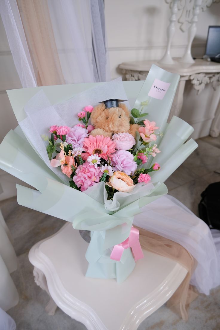 a bouquet of flowers with a teddy bear in the middle sitting on a chair next to a window