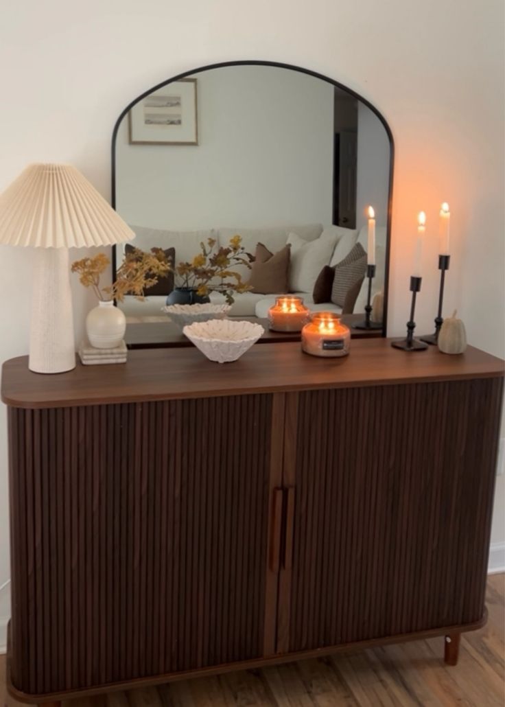 a living room with a couch, mirror and candles on top of the dresser in front of it