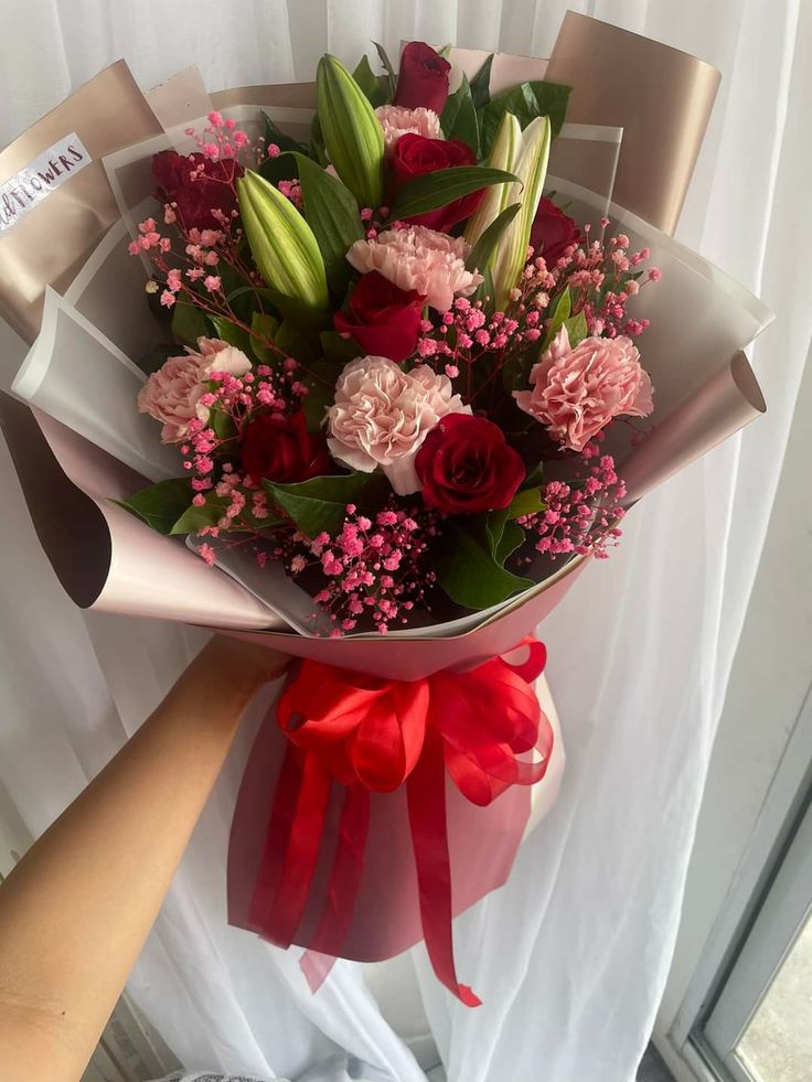 a bouquet of flowers is wrapped in red and pink paper with a ribbon around it