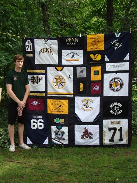 a young man standing next to a quilt made from sports jerseys on display in the woods