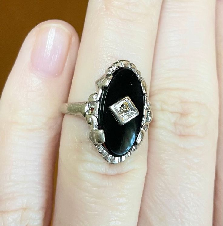 Gorgeous vintage art deco style ring! Featuring a 16x8mm onyx Cabochon and a 0.005 carat diamond; set in 14k solid white gold. Marked HNF 14K and acid tested This ring is a size 4 This ring weighs 4.50g This ring measures 19mm from the front; and 1.75mm from the back of the band. Vintage condition: Very Good (some minor wear on the band/setting; some tarnish on the inside of the setting). Onyx is a captivating black gemstone that is composed of microscopic quartz crystals and belongs to the chalcedony mineral group. The chemical composition of onyx is silicon dioxide (SiO₂), with varying amounts of iron oxide and other minerals that give it its unique color variations. Typically, onyx is black, but it can also be found in brown, red, and white. Onyx is a relatively hard mineral, with a Moh White Onyx, Quartz Crystals, Onyx Ring, Diamond Set, Iron Oxide, Art Deco Jewelry, Art Deco Style, Deco Style, Antique Style