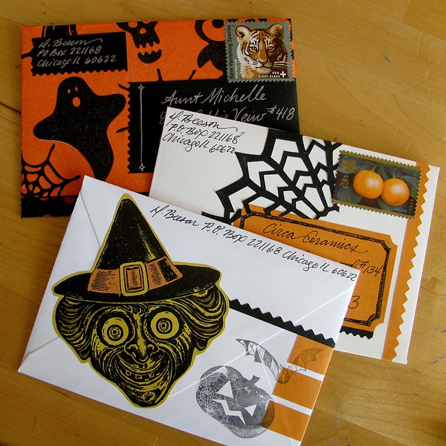 several envelopes decorated with halloween images and stamps on a wooden surface, including an orange witch's hat