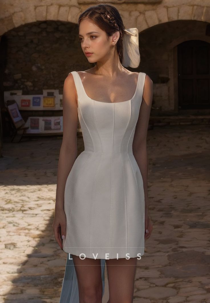 a woman in a short white dress standing on a cobblestone street with her hair pulled back