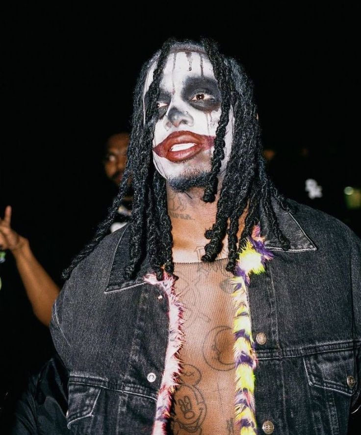 a man with dreadlocks and painted face standing in front of other people wearing makeup