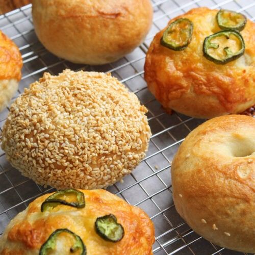 several baked goods are on a cooling rack, including bagels and muffins