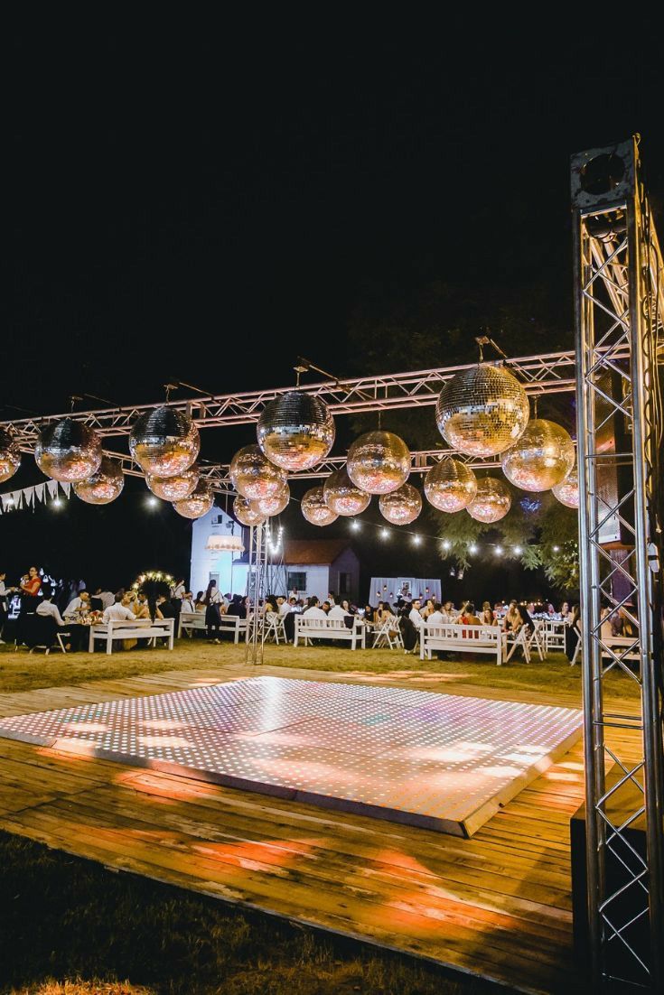 an outdoor dance with disco balls hanging from the ceiling and people sitting at tables around it