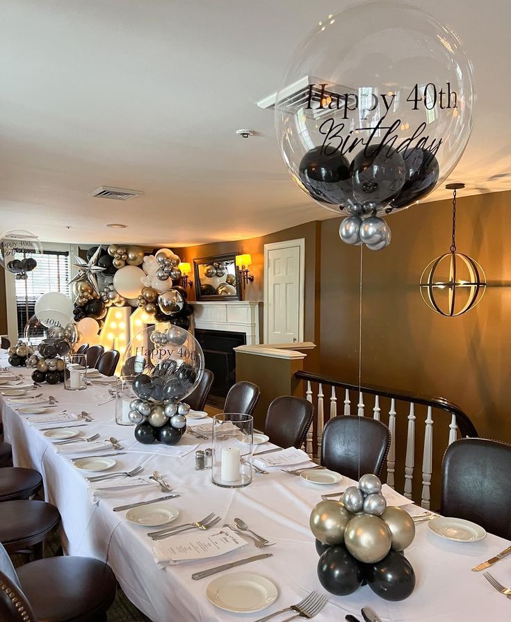 a table set for a birthday party with silver and black balloons, plates and napkins