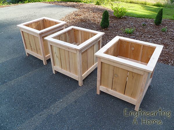 three wooden planters sitting next to each other on top of a gravel road in front of some bushes