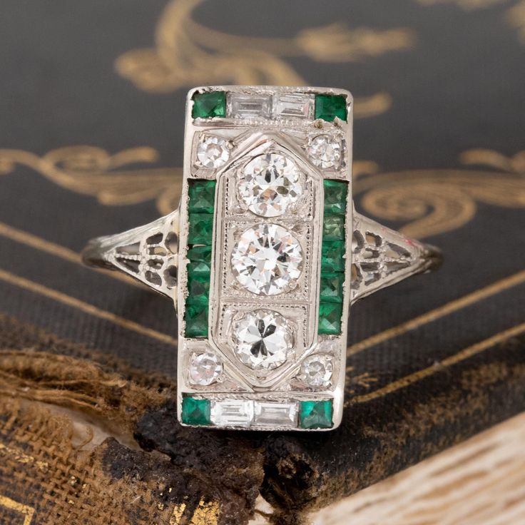 An Art Deco dinner ring studded with Old European cut diamonds, step cuts, and juicy green emeralds! This ring is full of impeccable detail, not to mention she covers up a significant amount of finger real estate! The color combination of diamonds and green emeralds is one that we cannot help but love, especially when set in an original Deco-era beauty. 18kt white gold Size 7.5 & fully resizable Diamond Measures: 5.67 x 5.67 x 3.94 mm Diamonds are estimated to be G/I colors & VVS/VS clarities. G Fine Jewelry Green Emerald Ring With Single Cut Diamonds, Art Deco Green Ring, Gia Certified, Art Deco Green Ring Gia Certified, Green Diamond Ring With Single Cut Emerald Shape, Green Emerald Cut Diamond Ring With Single Cut Diamonds, Green Diamond Platinum Ring Fine Jewelry, Vintage Green Diamond Platinum Ring, Vintage Green Diamond Ring In Platinum, Luxury Green Emerald Ring With Single Cut Diamonds