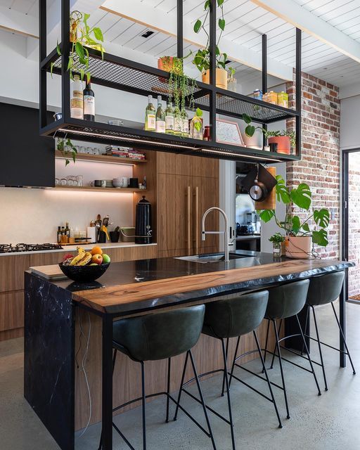 a kitchen with an island and bar stools in front of the counter, surrounded by potted plants