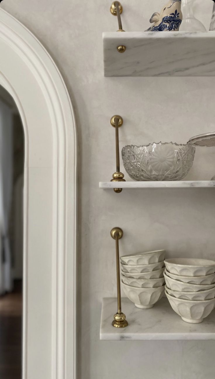 the shelves in this kitchen are filled with bowls and plates, along with brass handles