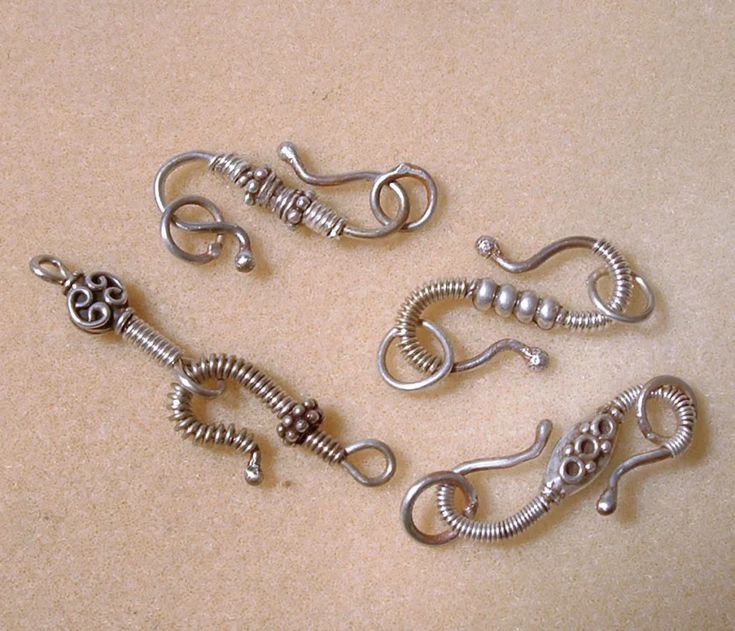 four silver metal hooks on top of a beige surface with beads and chains attached to them