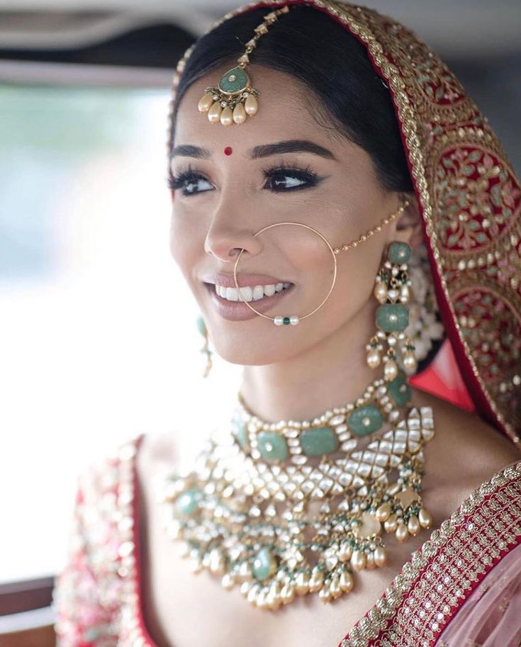 a woman in a red and gold bridal outfit with jewelry on her head, smiling