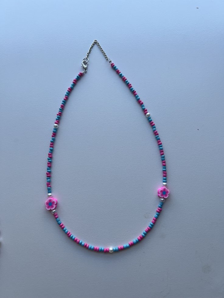 This is a seed bead necklace with a very fun and colorful pattern. It's handmade with a pink and blue pattern and 2 pearls and 2 flower charms.  - We used 2mm beads  - It has an adjustable chain  - The flower charms match the color scheme to make it more aesthetic  - It's very colorful, bright, and pretty  - It's on the girlier side but our shop will have more variety in the future  - The length is 16.5 inches but you can adjust it to your liking Beaded Multicolor Flower Necklace For Beach, Colorful Bead Flower Necklace For Beach, Colorful Beads Flower Necklace For Beach, Pink Spacer Bead Necklaces For Festivals, Pink Spacer Beaded Necklace For Festivals, Pink Spacer Beads Necklace For Festival, Multicolor Beaded Chain Flower Necklace, Blue Beaded Necklace With Flower Pendant, Flower Shaped Beaded Necklaces For Jewelry Making