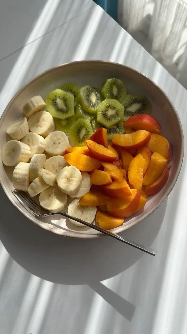 a bowl filled with sliced up fruit on top of a white table next to a window