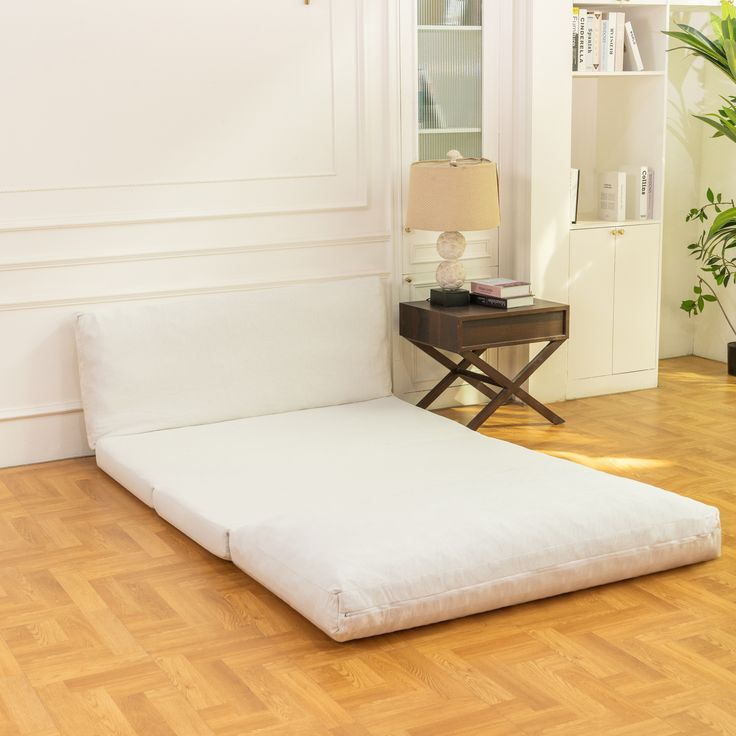 a white bed sitting on top of a hard wood floor next to a table with a lamp