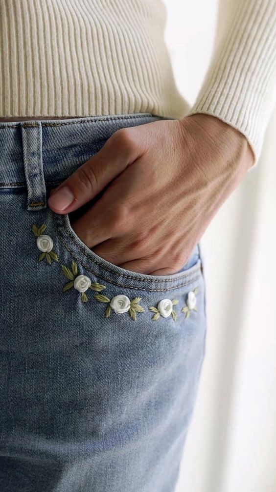 a woman is wearing jeans with flowers on the side and her hand in her pocket