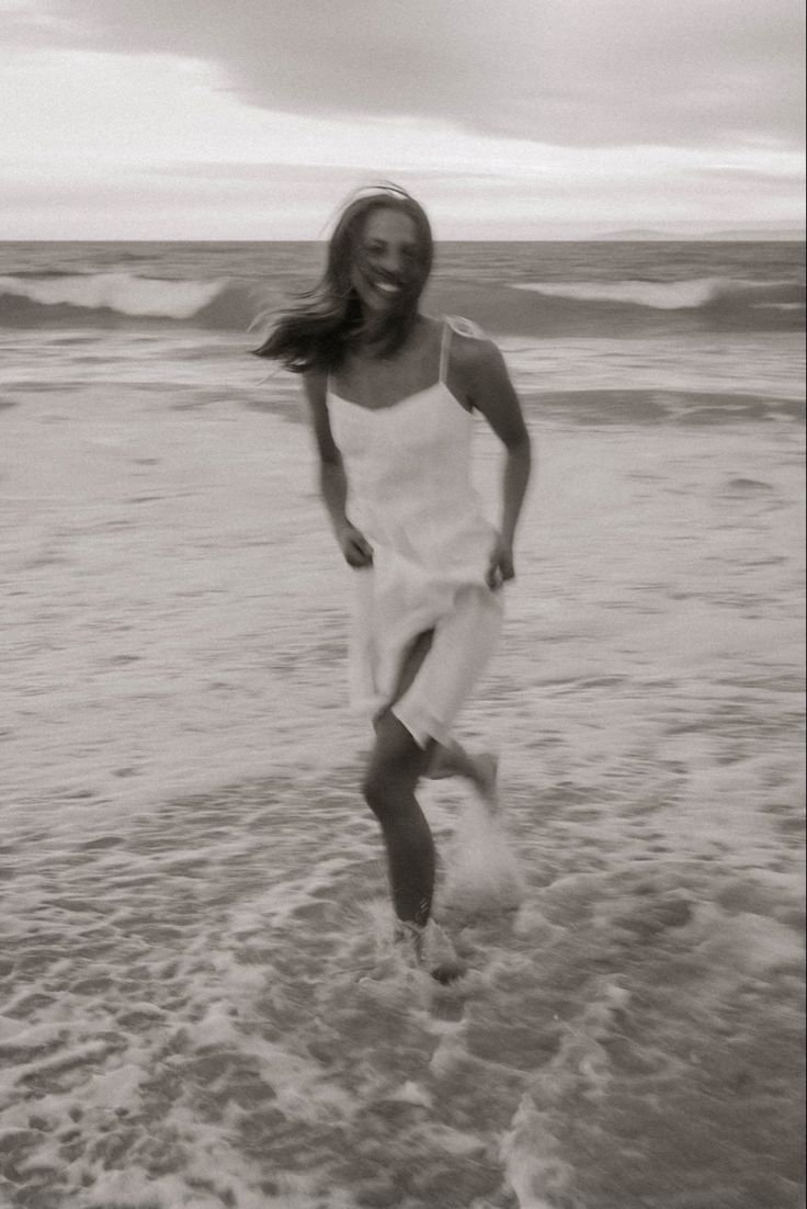 black and white photograph of woman running in the water at the beach with her hair blowing in the wind