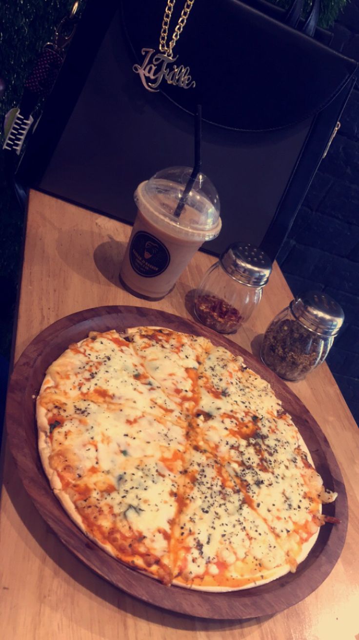 a large pizza sitting on top of a wooden table next to a cup of coffee