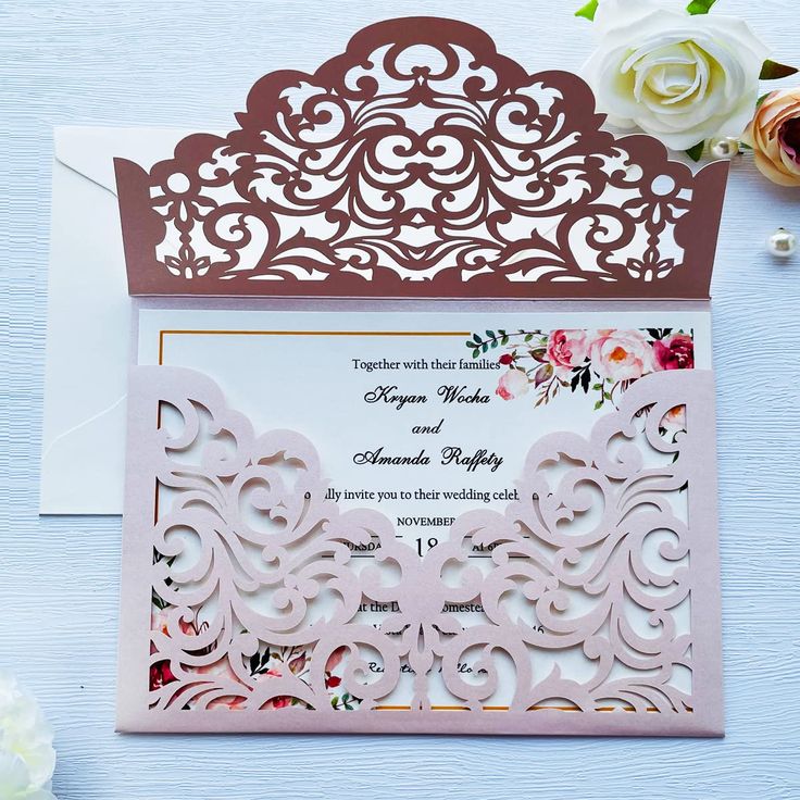 an ornate laser cut wedding card on a table with flowers in the background and white envelope