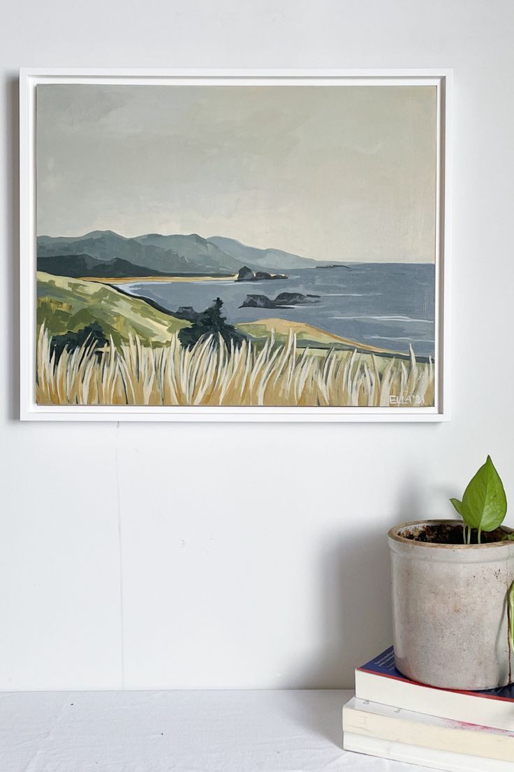 a painting hanging on the wall above a potted plant next to books and a book