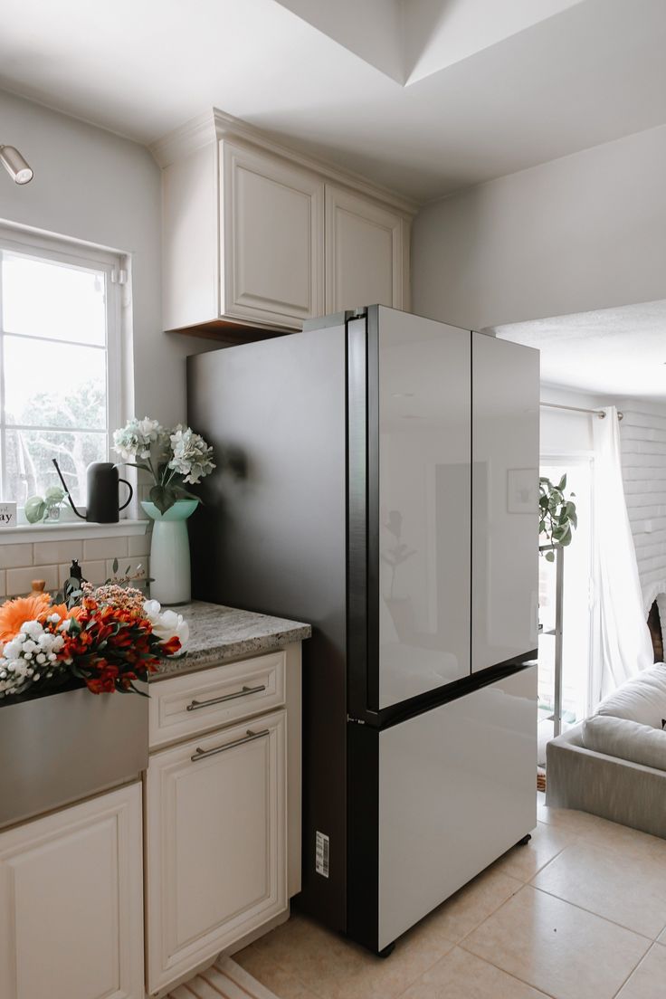 a kitchen with white cabinets and flowers on the counter top next to an open refrigerator