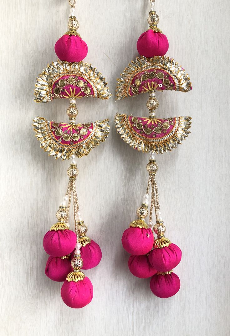 two pairs of pink and gold earrings hanging from hooks on a white surface with beads