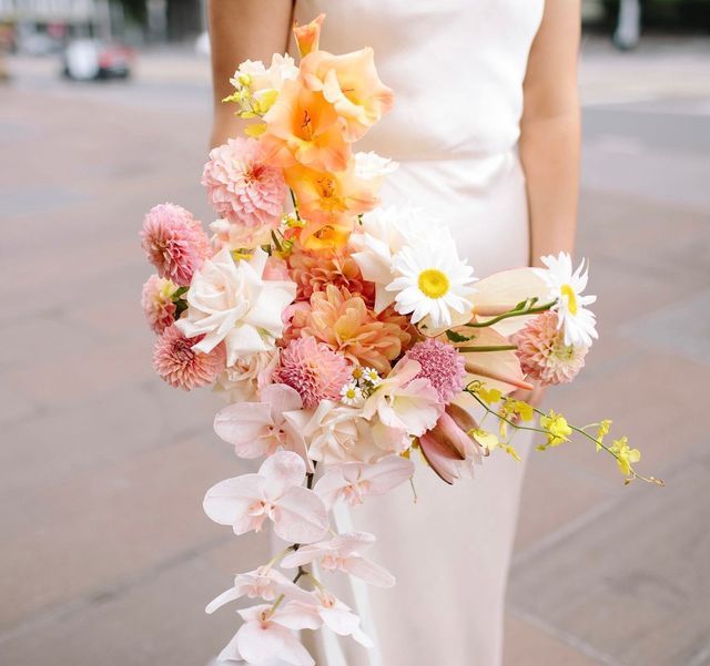 a woman in a white dress holding a bouquet of pink and yellow flowers on her wedding day