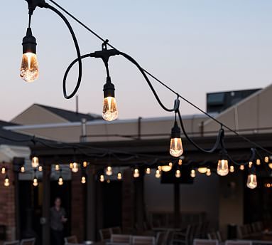 several light bulbs are hanging from a string on an outdoor dining room patio at dusk