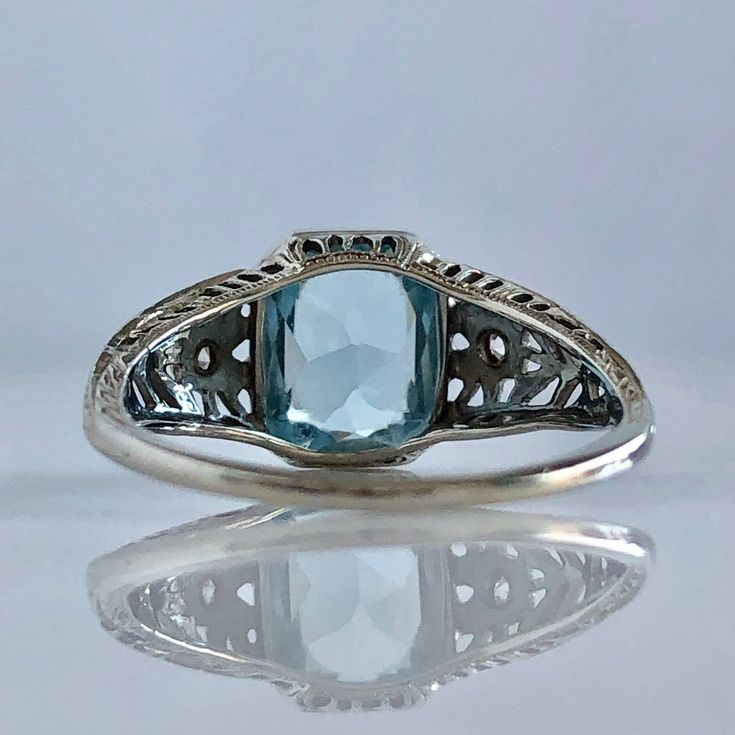 Details: Beautiful Edwardian Aquamarine & Diamond 18K white gold filigree ring. The ring has a sweet floral pattern on the sides of the filigree, and the diamonds are the center of the side flowers. The aquamarine measures 9mm x 7mm, and the two diamonds measures 2mm each. The ring is stamped 18K on the inside of the band. Measurements: Ring measures a size 7 1/4 US. It can be re-sized for a fee. Condition: The overall all condition of this ring is very good, with some very slight wear on th Fine Jewelry Sapphire Ring For Wedding With Intricate Design, Sapphire Ring With Intricate Design For Wedding, Wedding Sapphire Ring With Intricate Design, Elegant Oval Engraved Ring With Intricate Design, Wedding Engraved Diamond Ring With Gemstone, Luxury Oval Filigree Ring With Intricate Design, Elegant 14k Gold Engraved Filigree Ring, Antique Cushion Cut Rings For Formal Occasions, Elegant Oval Filigree Ring For Formal Occasions