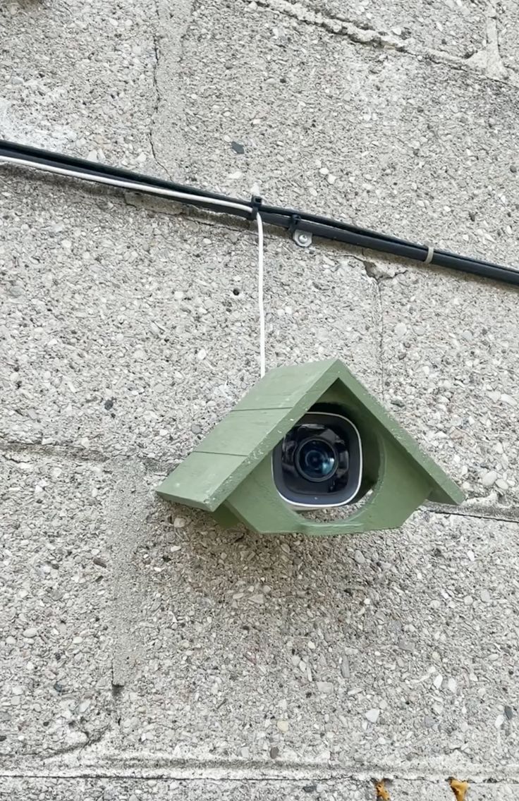 a birdhouse hanging on the side of a building with a camera attached to it