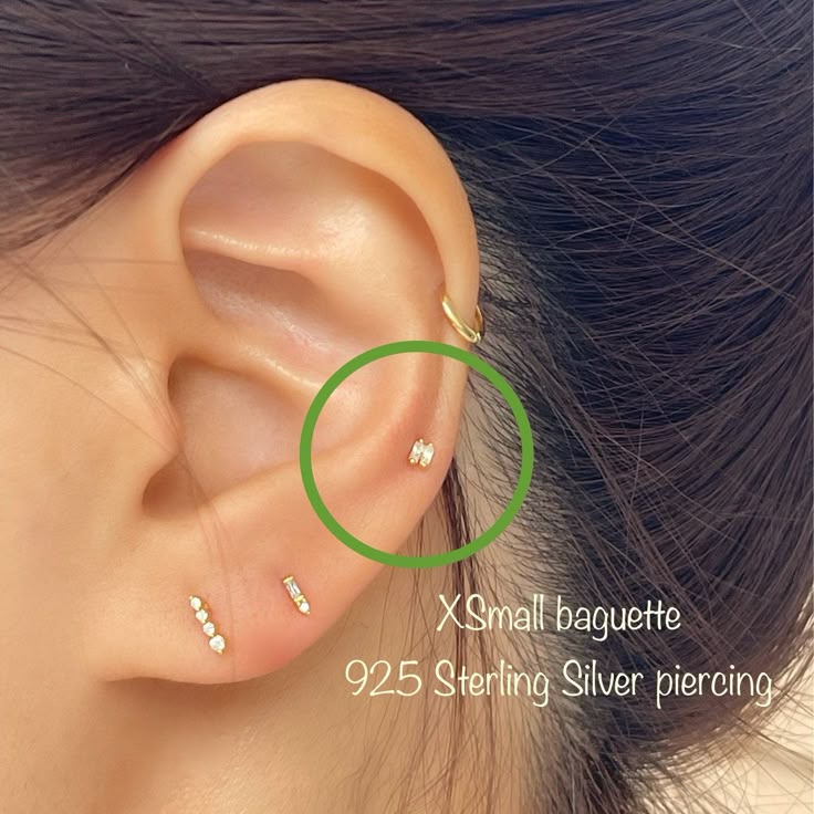 an ear piercing with three small white stones on the middle part of it, and a green circle at the end