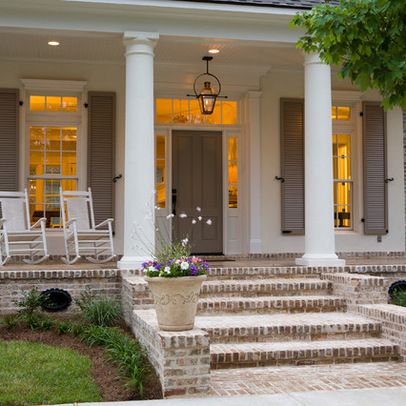 the front porch of a house with white pillars and two chairs on it's steps