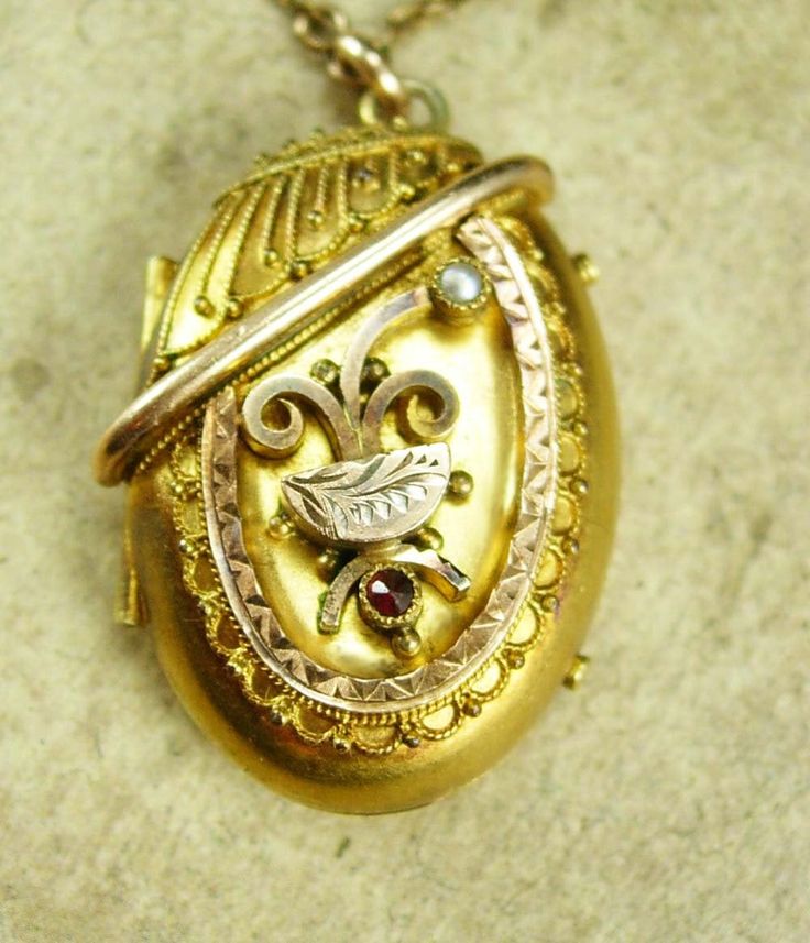 "I don't think I have seen a more ornate antique locket than this one. Using mixed metals of rose gold filled and yellow gold filled it is like a miniature piece of art. layers upon layers of detailing that are just magnificent. The locket has a rose gold center frame that is diamond etched and an ornamental piece that drapes over the lavish scroll work. A seed pearl rises up out of one oft he scroll works as if to represent a flower. A single garnet resides under the larger etched half moon. Th Victorian Filigree Locket Necklace In Yellow Gold, Victorian Yellow Gold Locket Necklace With Filigree, Victorian Filigree Yellow Gold Locket Necklace, Gold Locket Necklace With 17 Jewels For Wedding, Antique Gold Hallmarked Locket Necklace, Victorian Yellow Gold Pendant Locket Necklace, Victorian Oval Necklace With Antique Finish, Ornate Oval Locket Necklace From Vintage Collection, Victorian Oval Necklaces With Antique Finish