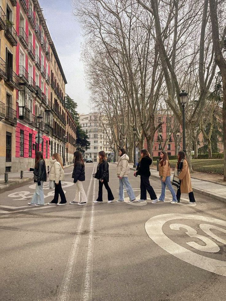 several people walking across the street in front of some tall buildings and trees with no leaves on them